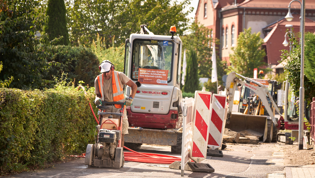 Ein Bauarbeiter und ein Bagger bei Tiefbauarbeiten auf einer Strasse